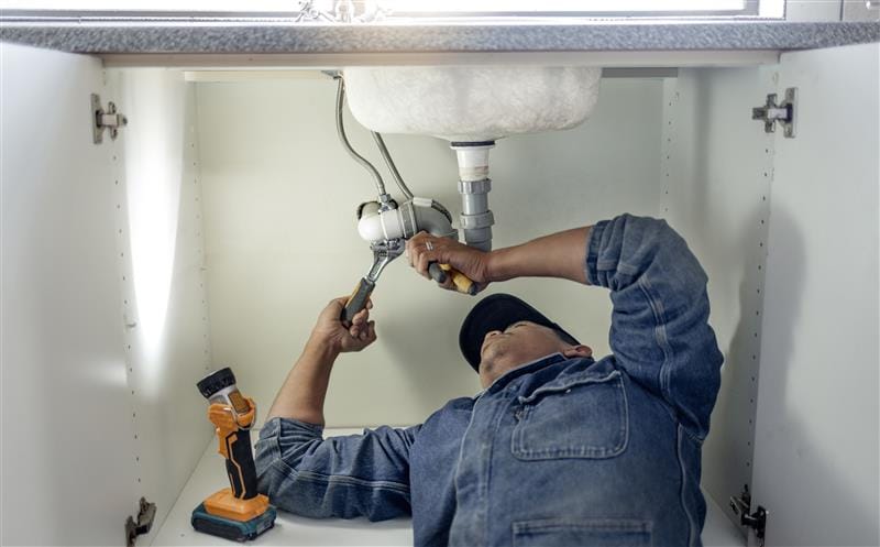 Plumber repairing pipes beneath a bathroom sink in Upland