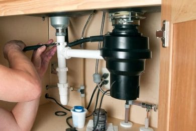 Plumber repairing a garbage disposal beneath a kitchen sink in Upland