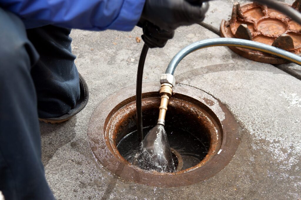 Plumber hydro jetting a sewer line through a manhole in Upland