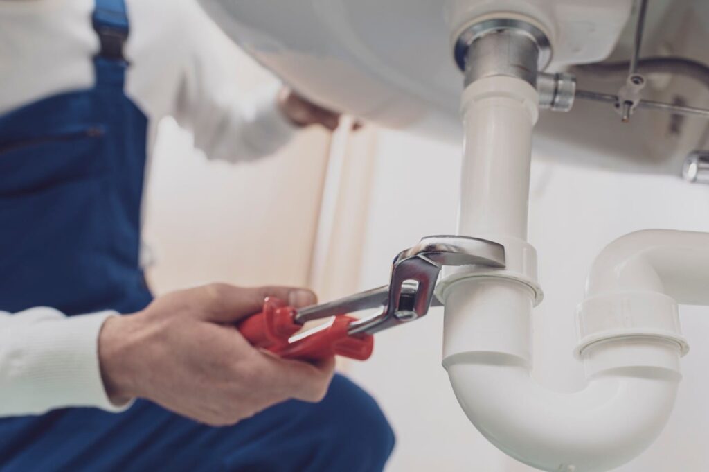 Plumber repairing a white drain pipe beneath a sink in Upland