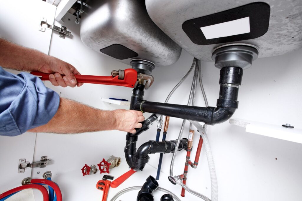 Plumber repairing drain pipes beneath a kitchen sink in Upland